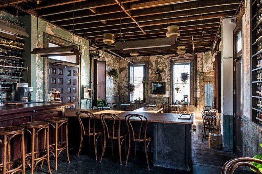 A rustic bar with wooden chairs, a bar counter, and shelves of bottles. 2