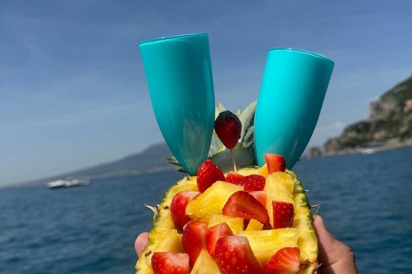 A hand holding a pineapple with fruit and two blue cups. 3