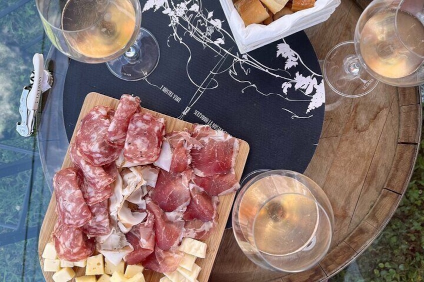 A wooden table with a charcuterie board, glasses of white wine, and a decorative placemat. 1