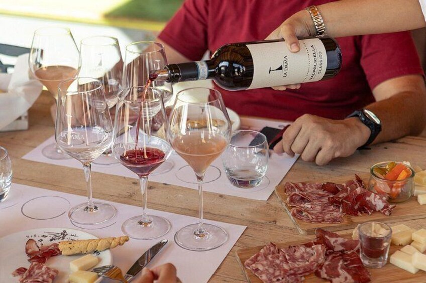 A person pouring wine into glasses, a cheese board with various cheeses, and a selection of cured meats on a table. 1
