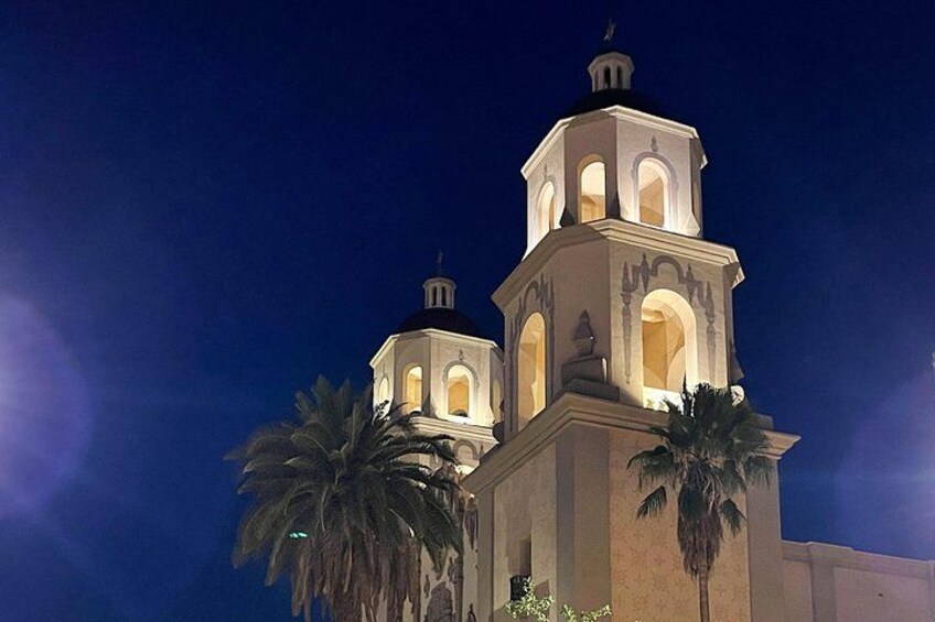 A night-time view of a building with two bell towers, palm trees, and a clear sky. 3