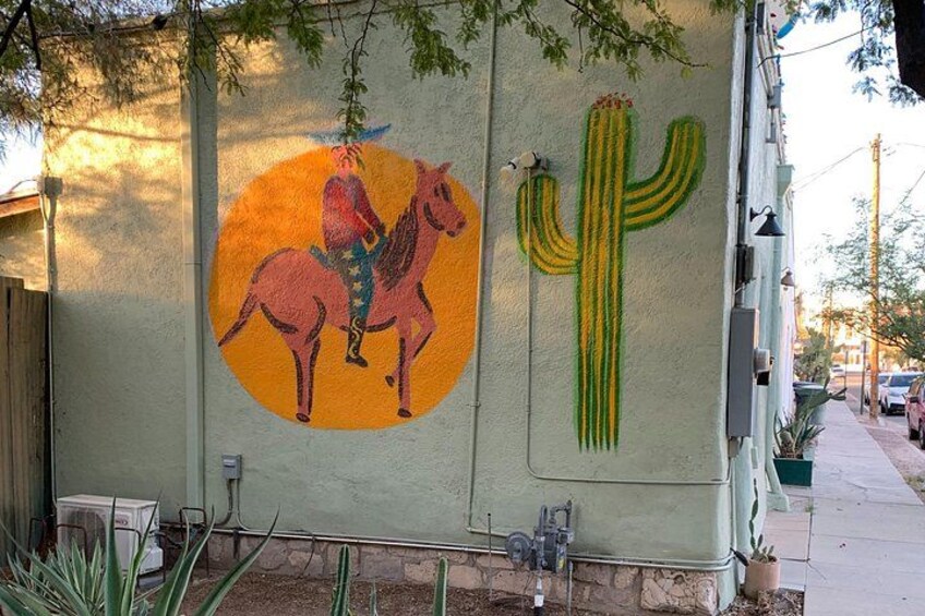 A mural of a person on a horse and a cactus on a building wall. 4