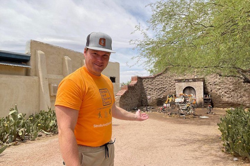 A person in an orange shirt standing in front of a historical building with a stone wall and an arched entrance. 3
