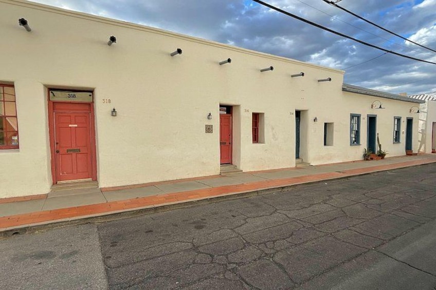 A row of single-story buildings with numbered doors, a red door on the left, and a clear sky. 2