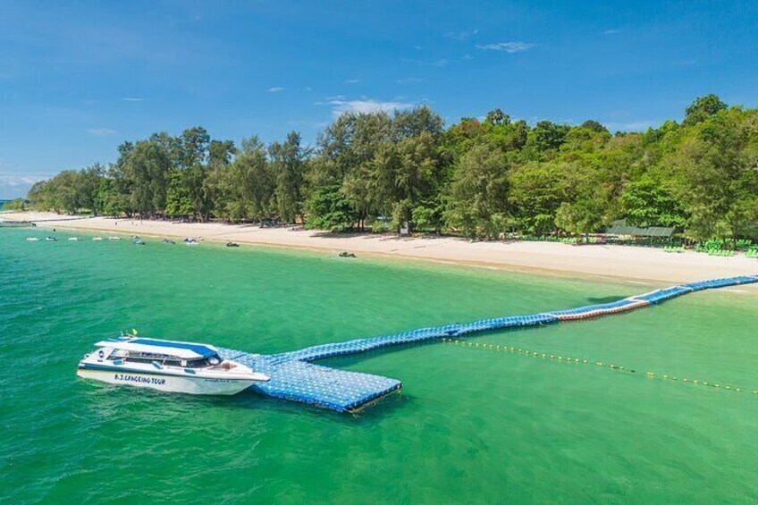 A boat anchored near a beach with a blue floating dock extending into the water. 3