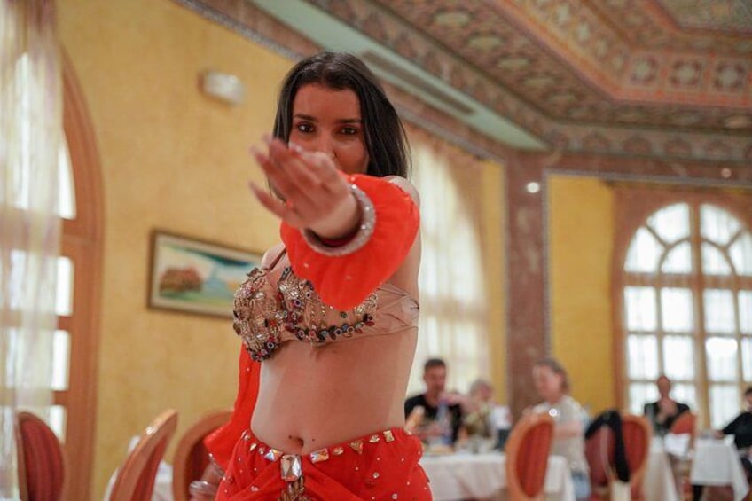 A person in a red outfit with a decorative top, standing in a room with ornate ceiling and large windows. 4