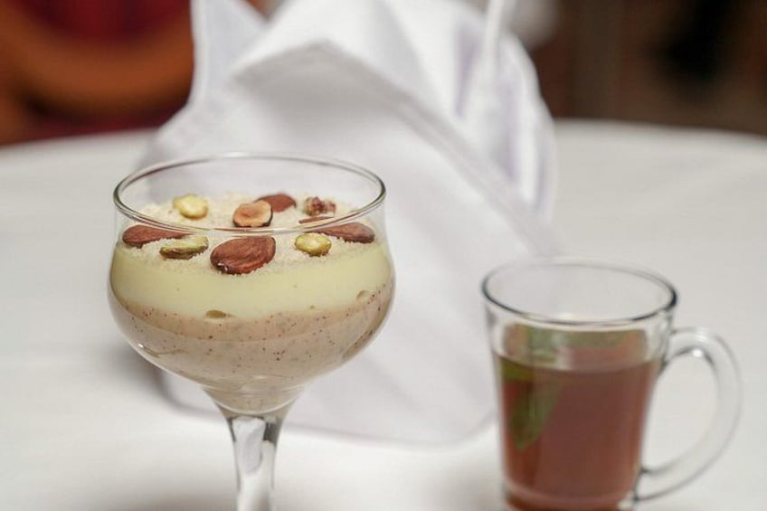 A dessert in a glass with nuts on top, next to a glass of tea. 2