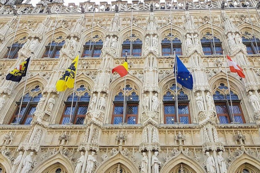 En bygning med detaljeret gotisk arkitektur, flere flag heriblandt EU-flaget, og statuer. 3