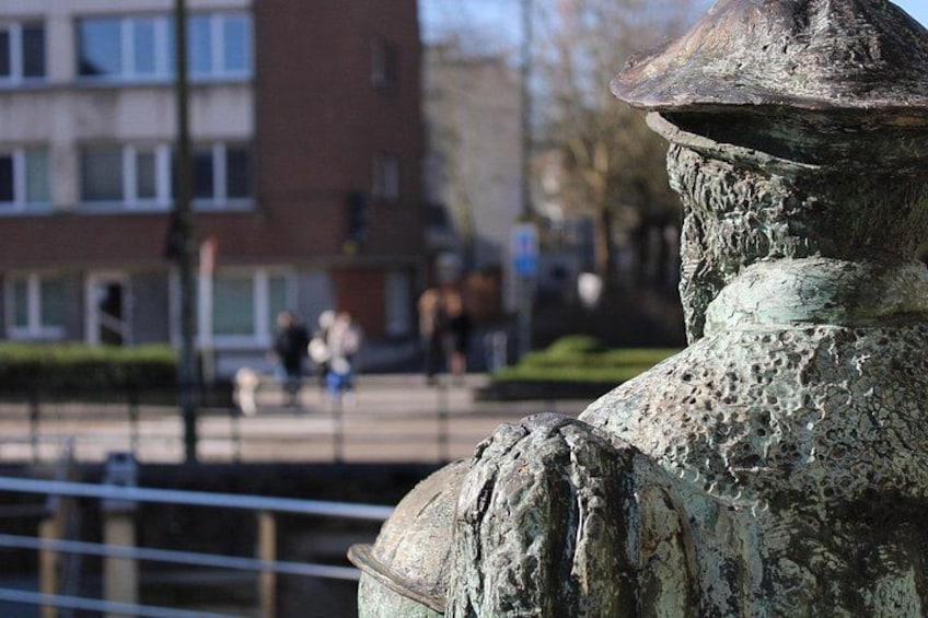 En vejrbidt statue med et hjelmlignende topstykke, foran en bygning og en fortov. 2