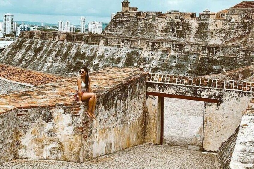 A woman sitting on a weathered stone wall with a cityscape in the background. 1