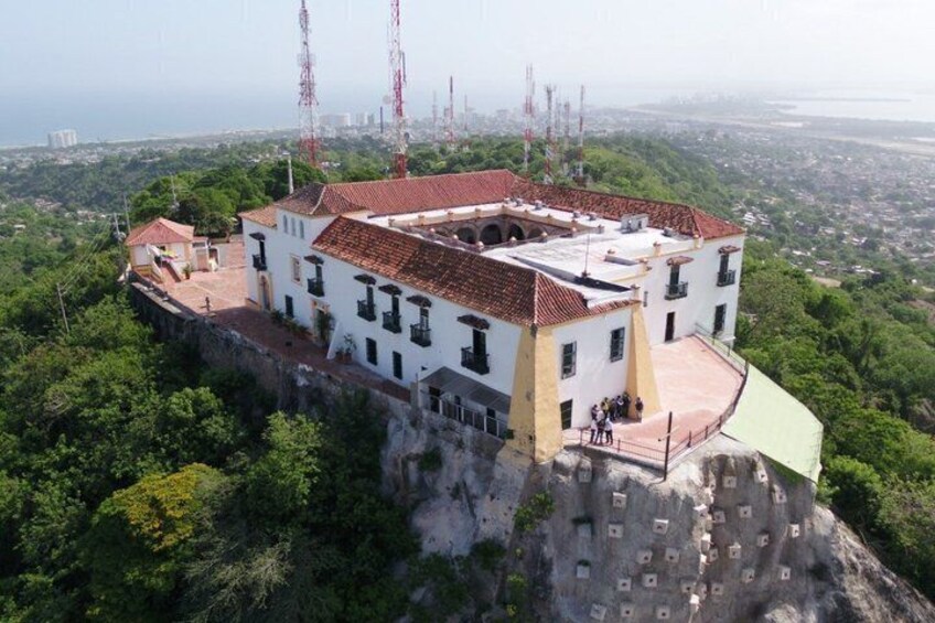 A white building with a red roof on a cliff overlooking a city. 3