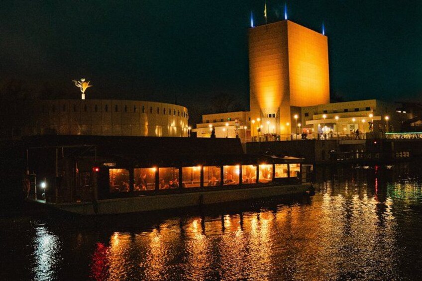 A nighttime view of a building with a large illuminated tower and a boat docked in the water in front. 5