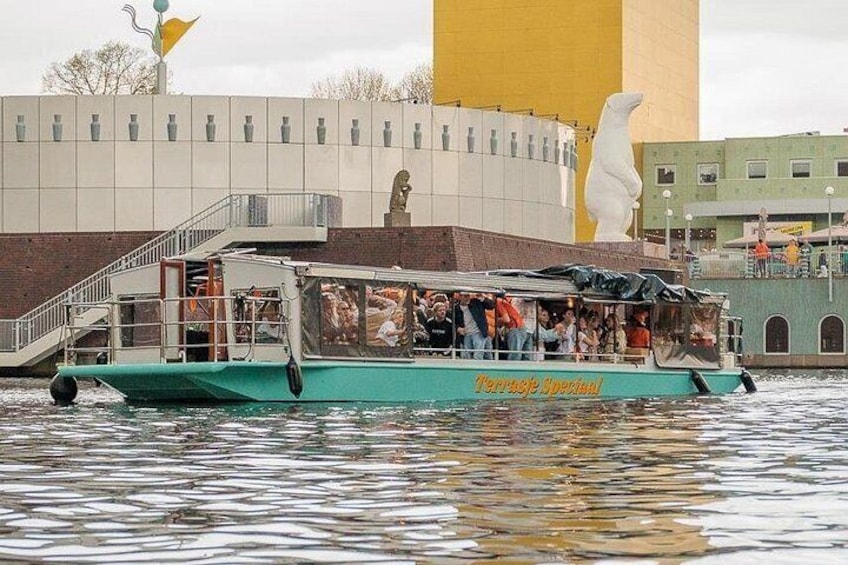 Un bote verde con gente a bordo, una estatua y un edificio con una torre amarilla. 1
