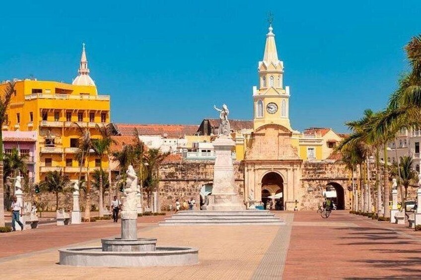 A plaza with a central monument, a clock tower, and surrounding buildings. 2