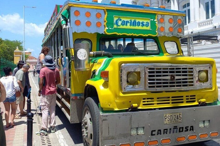 A colorful bus with the name 'Carinosa' on it, parked on a street with people standing nearby. 4