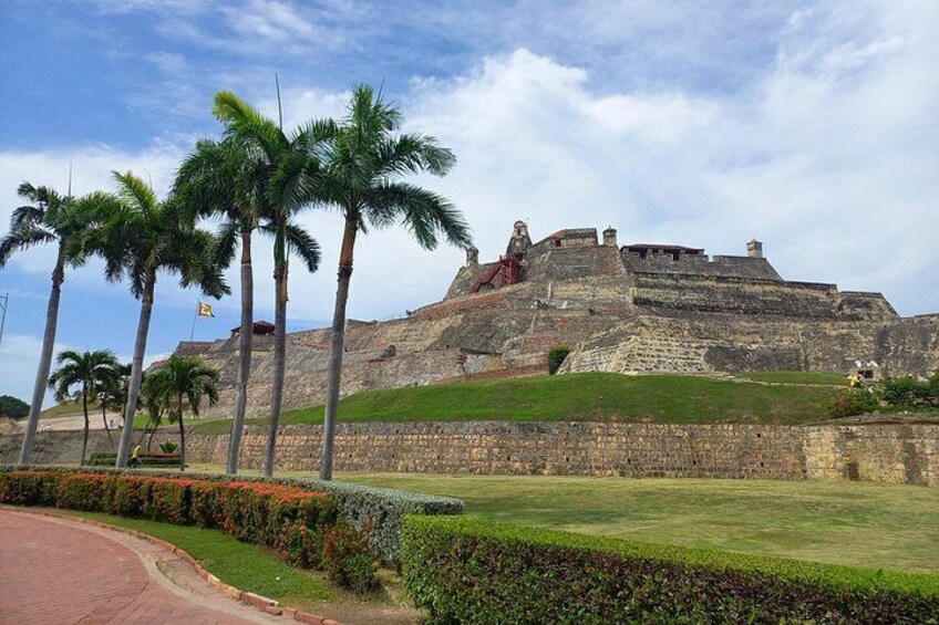 A historic fort with palm trees, a grassy area, and a clear sky. 2