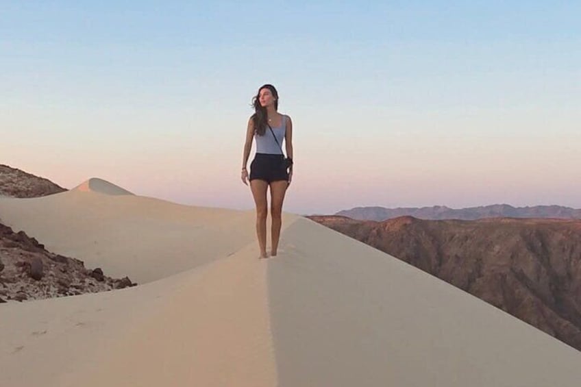 A person walking on a sand dune with a clear sky in the background. 1