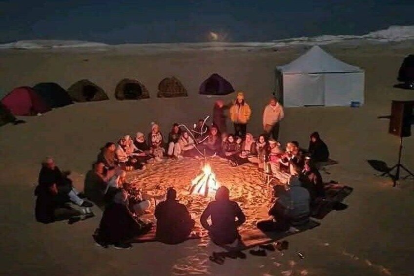 A group of people gathered around a campfire in a snowy landscape with tents in the background. 2