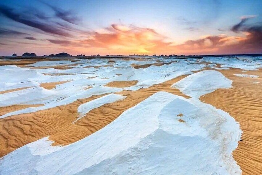 A desert landscape with snow-covered sand dunes and a sunset in the background. 3