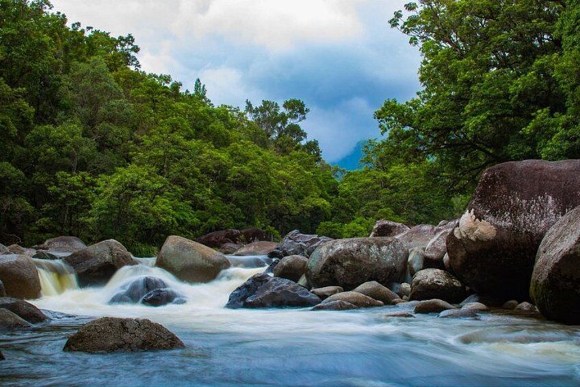 A river flowing through a forest with large rocks and dense green trees. 2