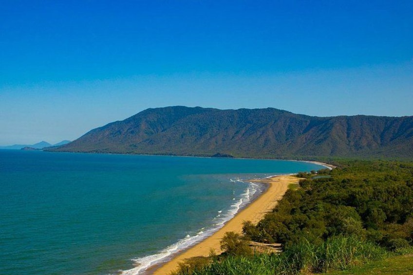 A coastal landscape with a beach, clear blue waters, and a mountain range in the background. 3