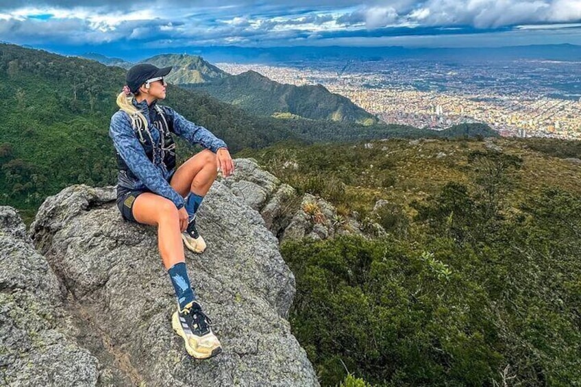 A person sitting on a rock with a cityscape in the background. 1