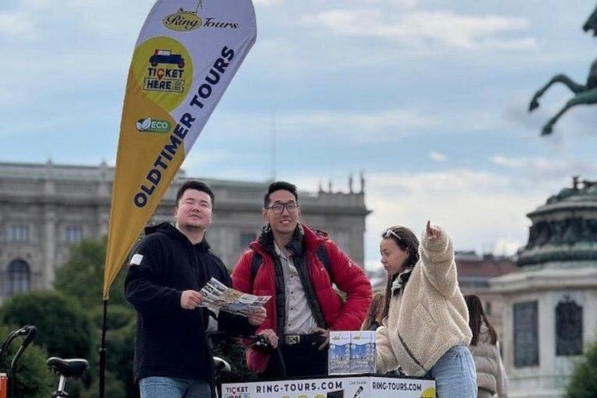 Un grupo de personas frente a un edificio histórico con una bandera que dice 'Oldtimer Tours'. 2