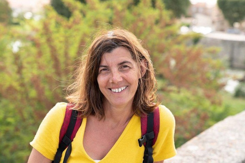 A person wearing a yellow top and a red backpack, standing outdoors with greenery in the background. 4