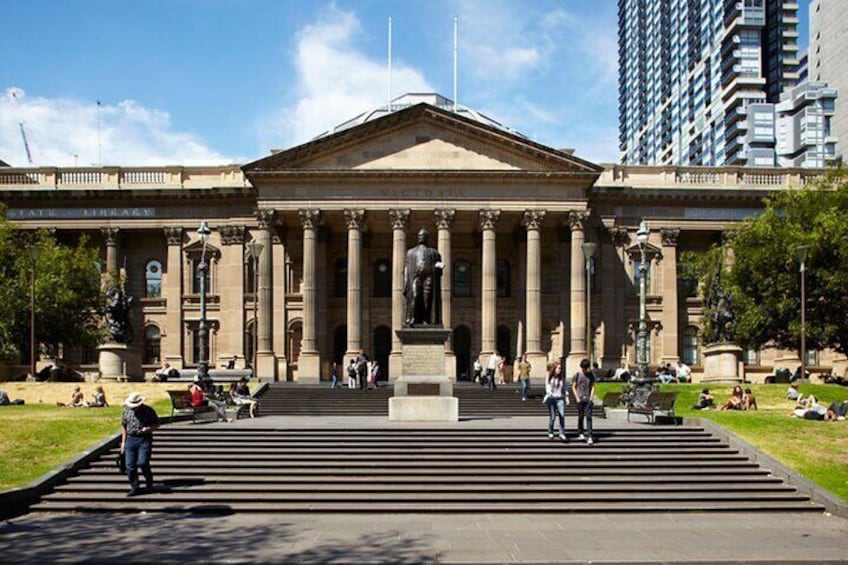 Un bâtiment de style classique, avec des colonnes, une statue à l’avant et des personnes assises sur les marches. 5