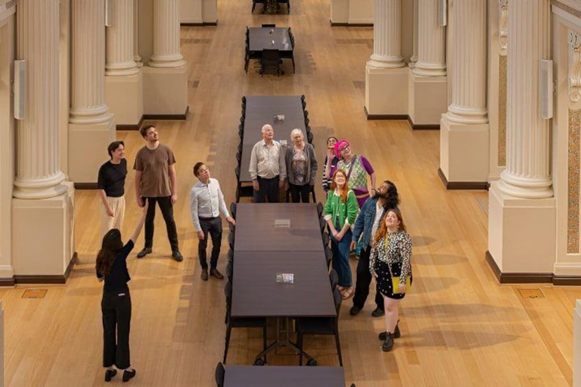 Un groupe de personnes se tient dans un grand hall orné de colonnes et de tables. 2