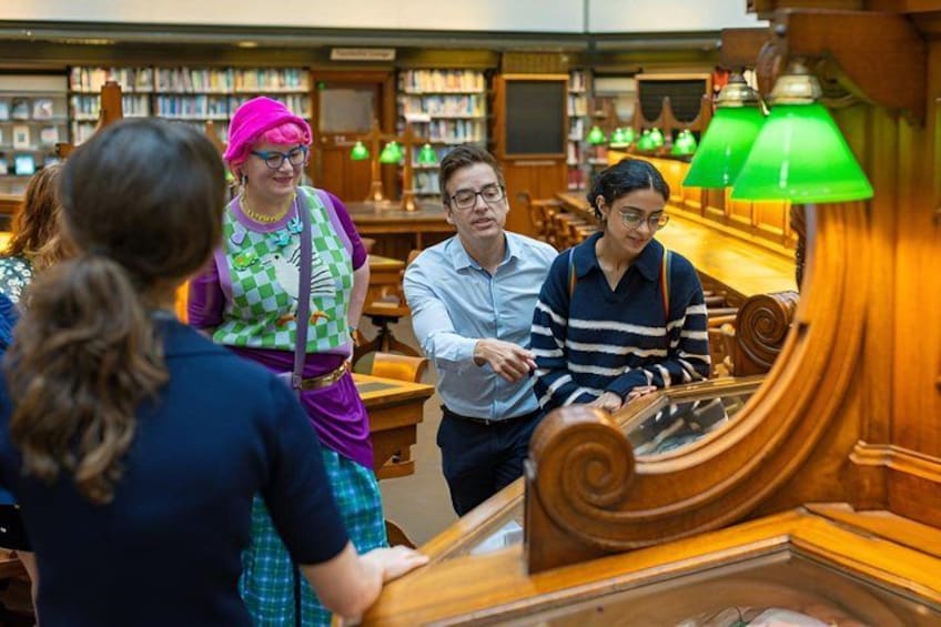 L'intérieur d'une bibliothèque avec des étagères, une table en bois et une lampe verte. 3
