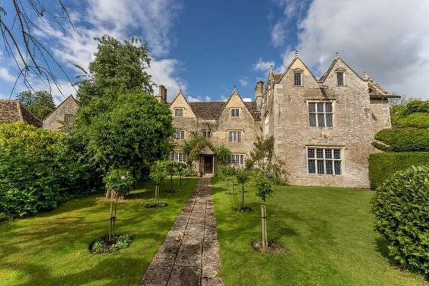 A stone manor with a well-manicured lawn and a central pathway leading to the entrance. 1