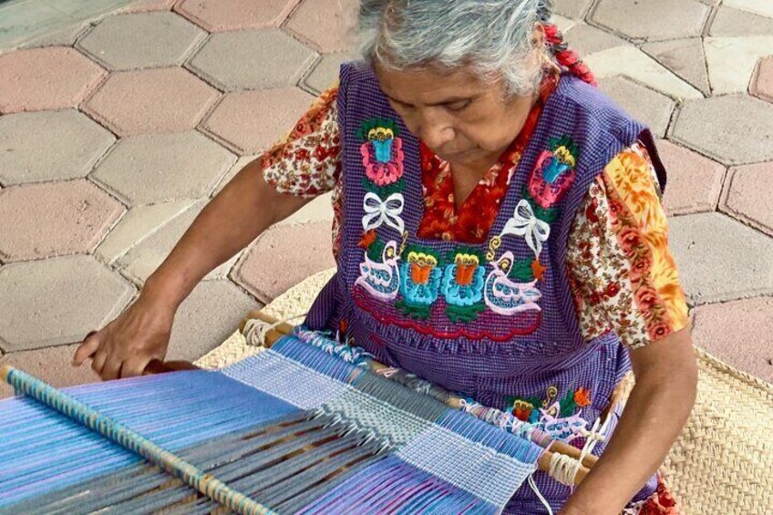 An elderly woman weaving on a loom with colorful patterns. 2