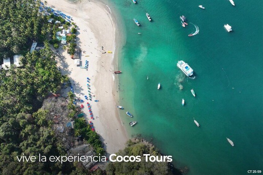 An aerial view of a beach with boats, umbrellas, and a clear turquoise sea. 2