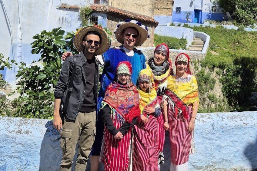 A group of people in traditional attire posing on a hillside with buildings in the background. 1