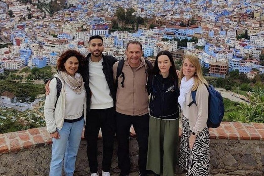 Eine Gruppe von Menschen steht auf einem Vorsprung und blickt auf eine dicht bebauchte Stadtlandschaft mit blau-weißen Gebäuden. 2