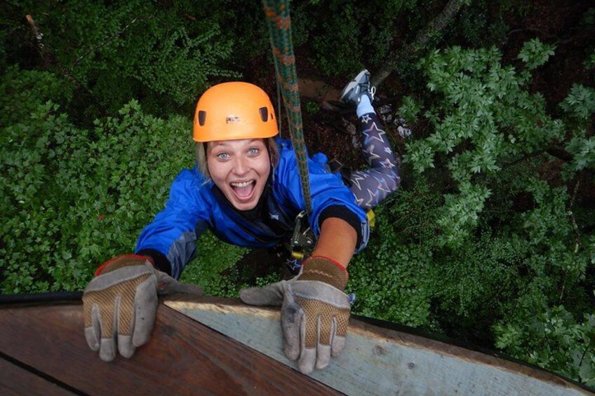 A person rappelling down a wooden surface with a harness and helmet. 3