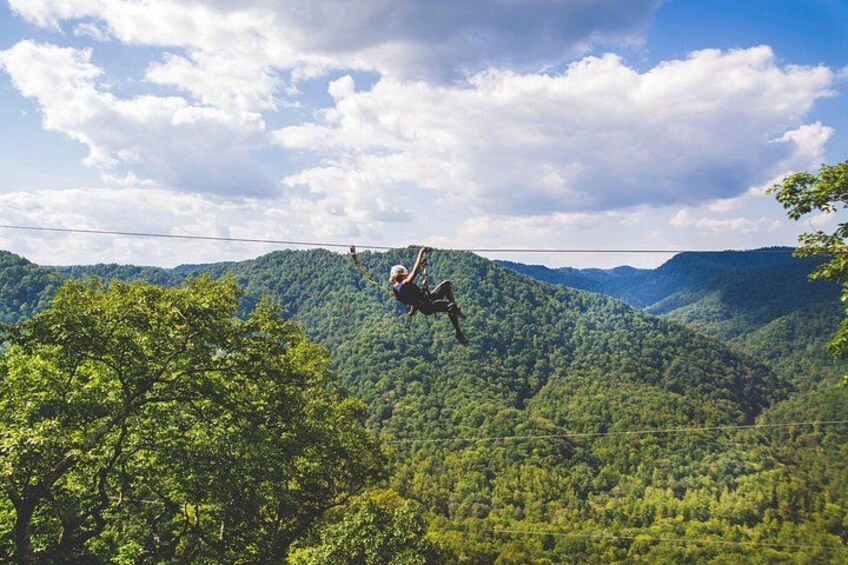 A person zip-lining over a forested mountain range. 1