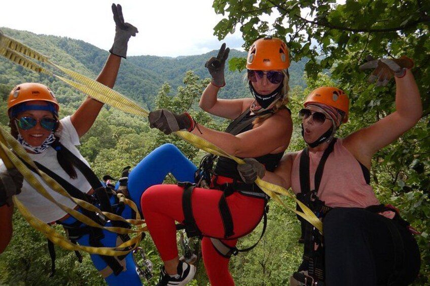 Three people engaged in a zip-lining activity, wearing helmets and harnesses, with a forested landscape in the background. 5