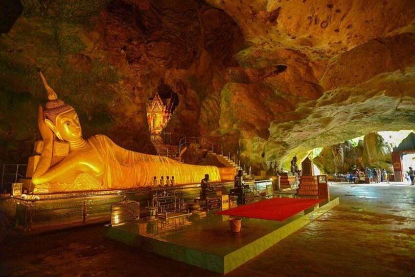 A reclining Buddha statue in a cave, with a small shrine and a red platform in front. 3
