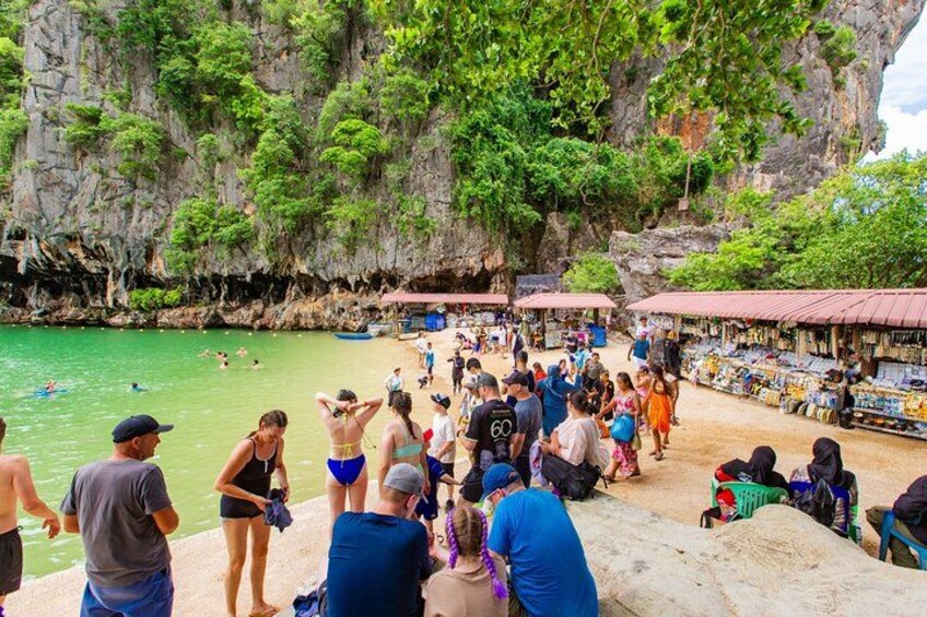 Une plage bondée, où l’on voit des gens se baigner et se tenir debout, entourée de falaises rocheuses et d’une végétation luxuriante. 3