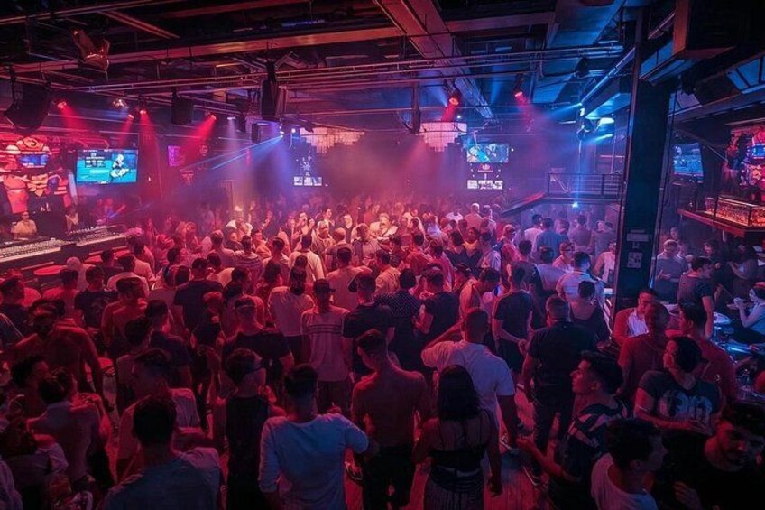 A crowded nightclub with people dancing and a DJ booth. 3