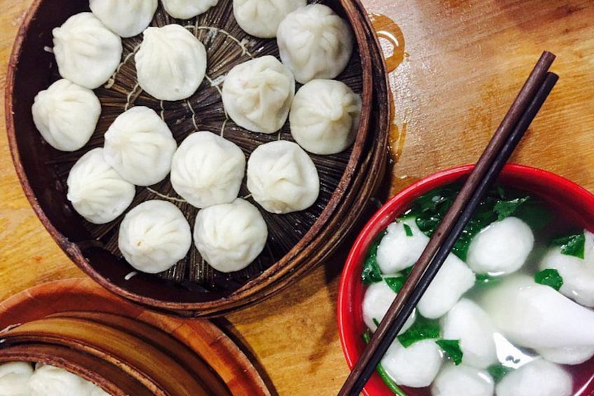 A wooden tray with steamed dumplings, a bowl of soup with dumplings, and chopsticks. 4