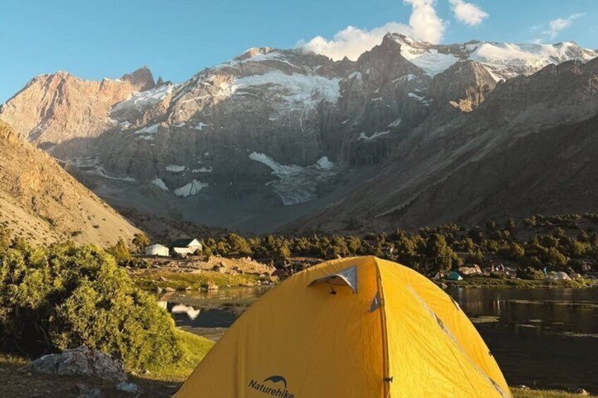 A yellow tent in a mountainous area with a lake and snow-capped peaks in the background. 3