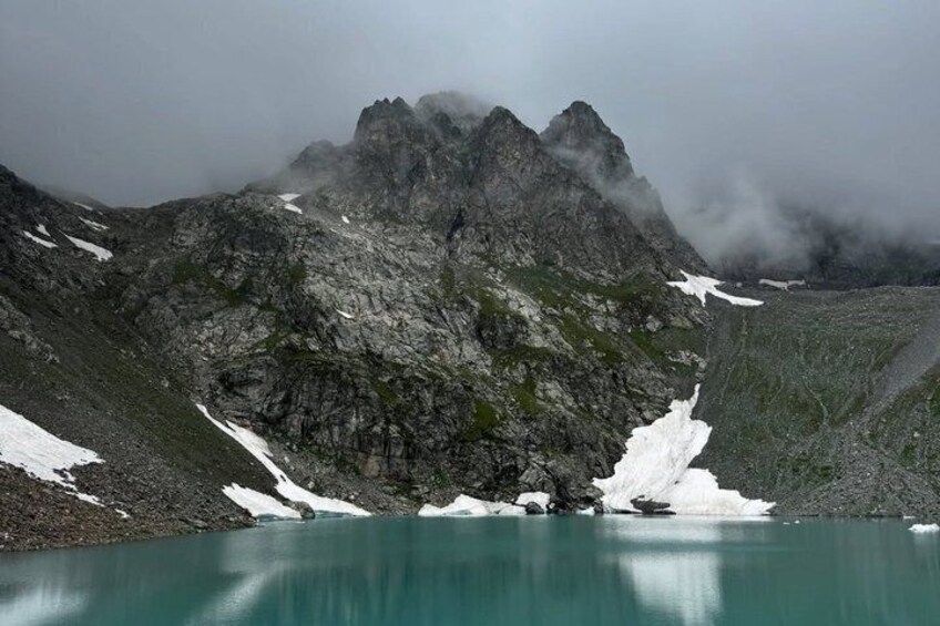 A mountain lake with snow patches and a rocky peak. 2