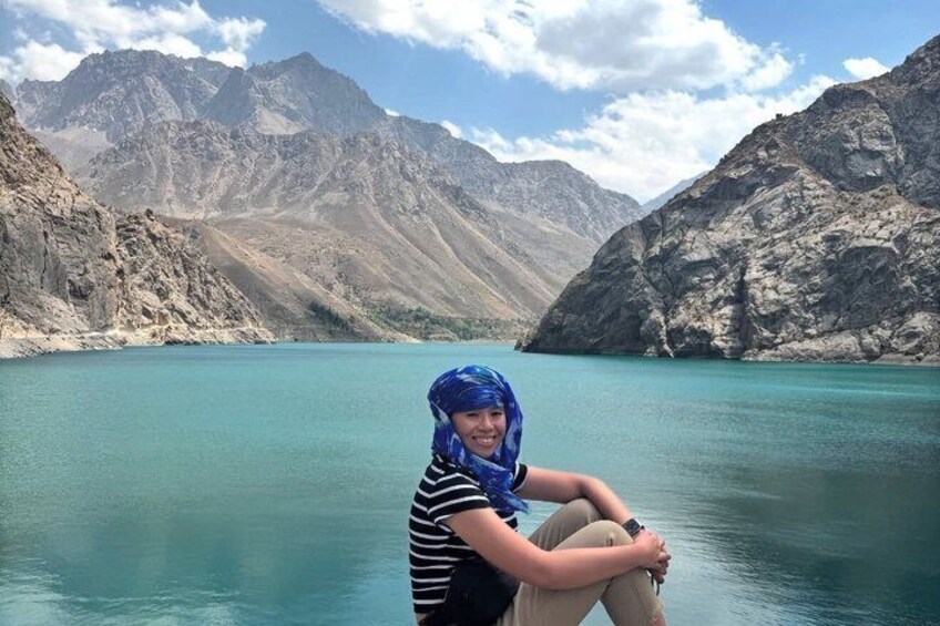 En person sidder ved en turkis sø med bjerge i baggrunden. 2