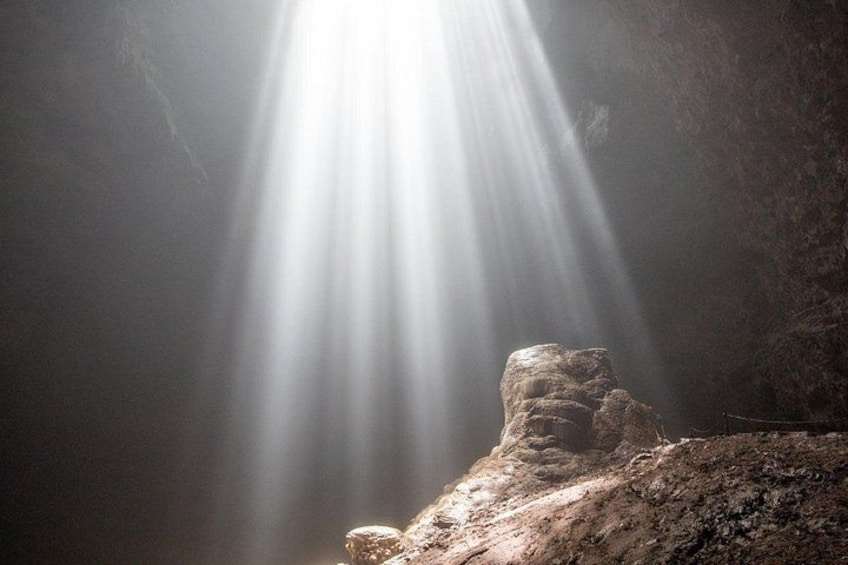 A cave with sunlight streaming through an opening, illuminating a rock formation. 2