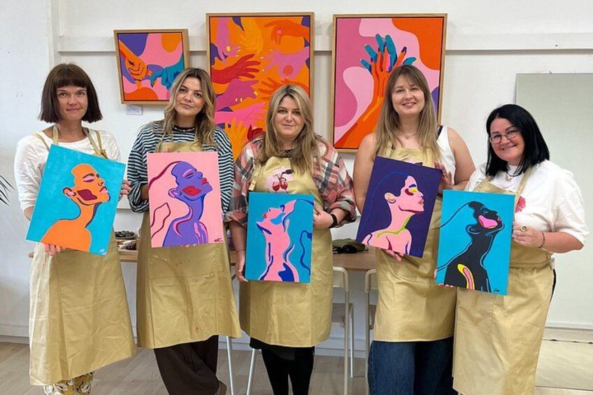 Fem personer holder farverige malerier i et atelier. 2