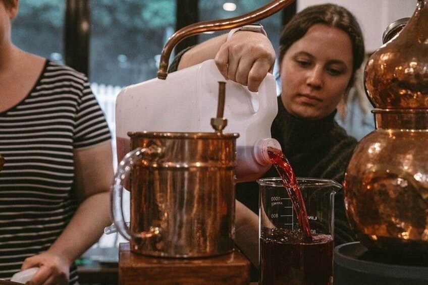A person pouring a red liquid from a jug into a copper pot. 4