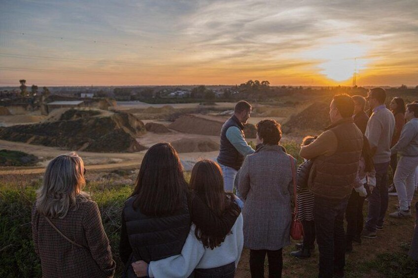 A group of people standing on a hill overlooking a landscape with mounds and a sunset in the background. 3
